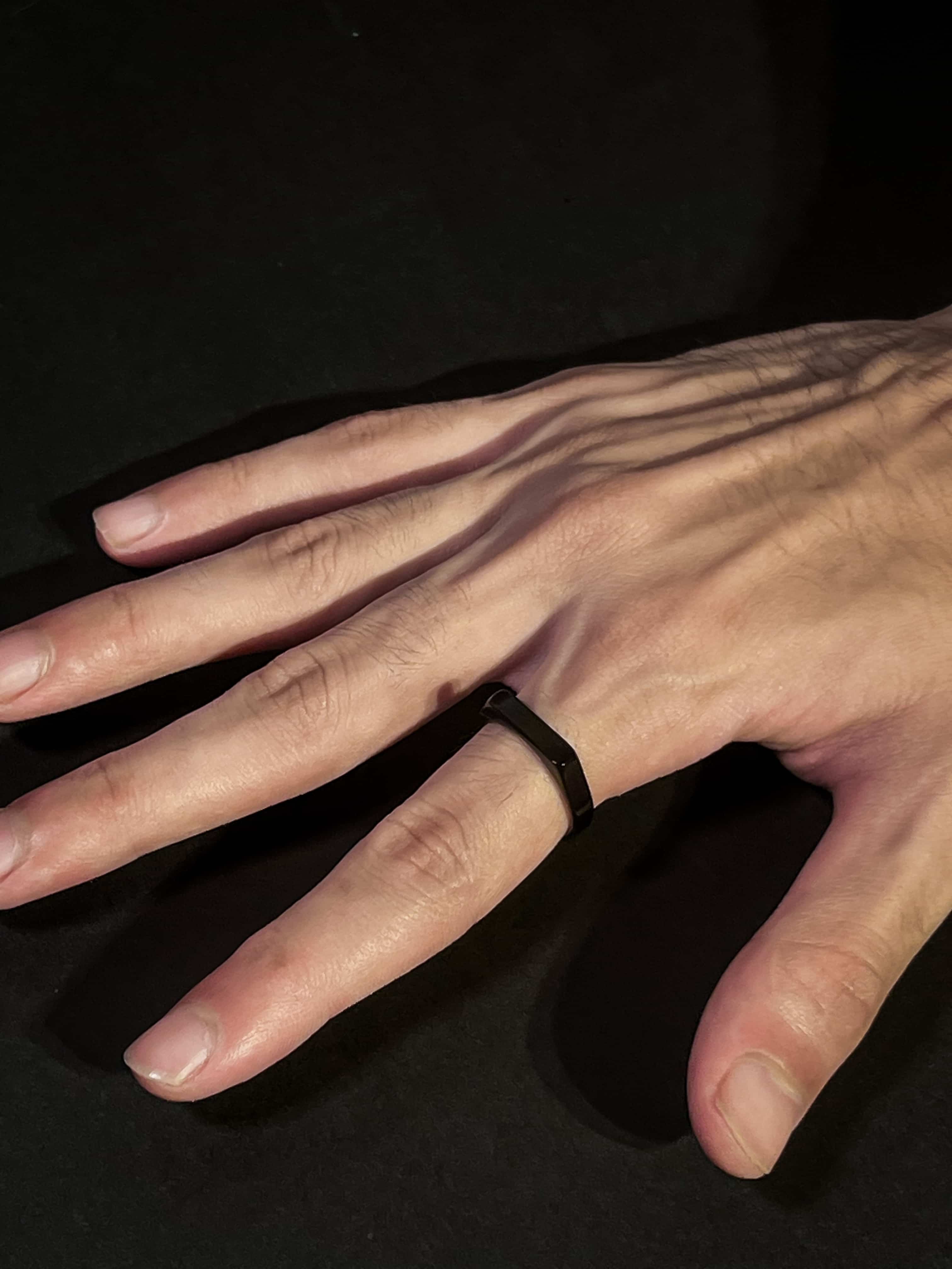 Hand wearing a black ring on a dark background