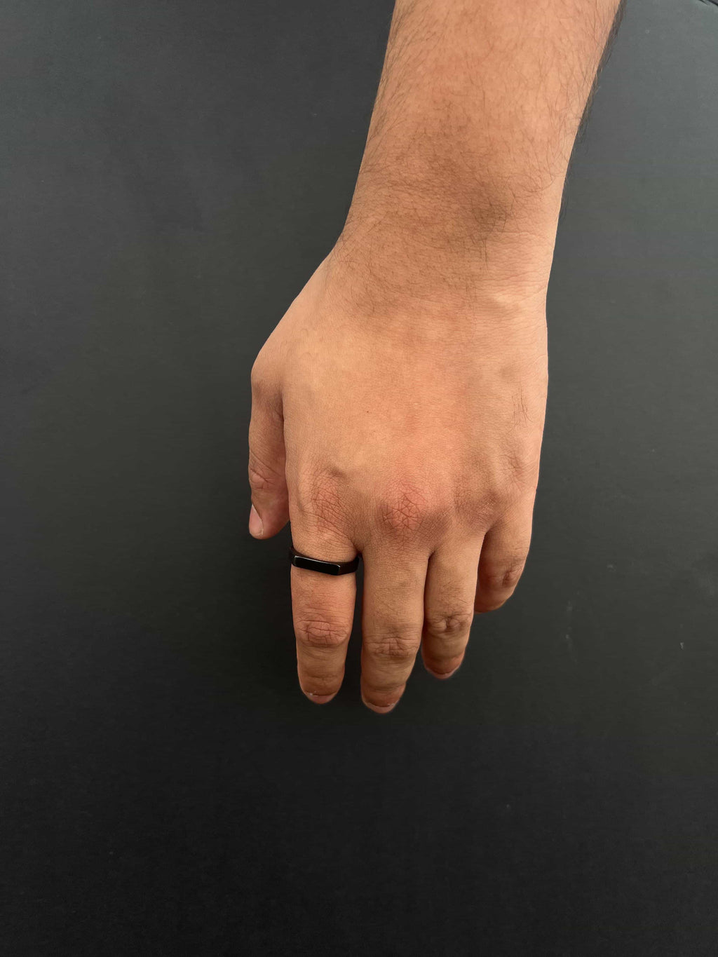 Hand wearing a black ring on a dark background