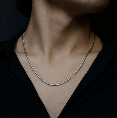 Silver necklace on a person wearing a black shirt against a dark background
