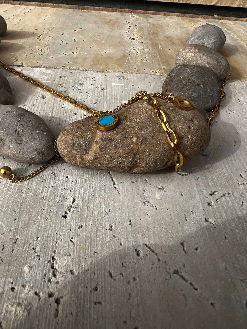 Gold necklace with a blue stone pendant on stones