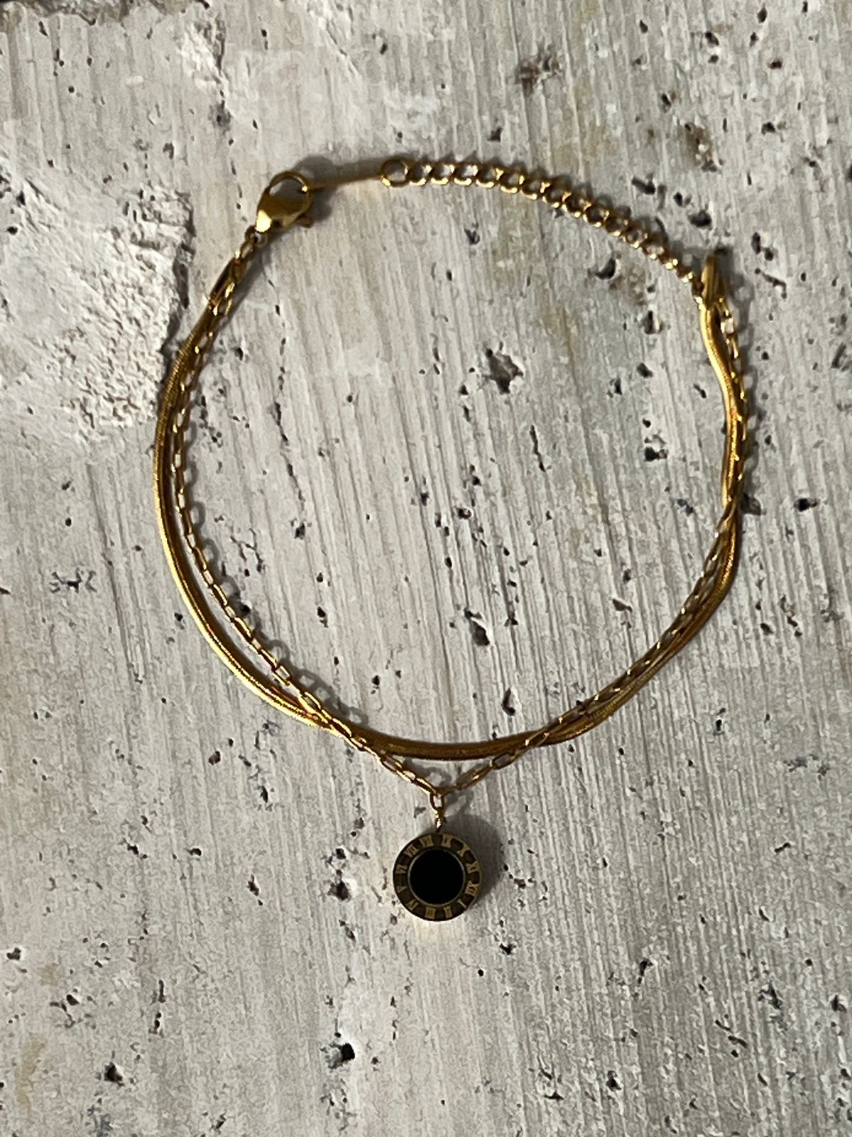 Black charm bracelet with a circular pendant on a minimalist gold chain — a modern fashion accessory and everyday wear bracelet for women.